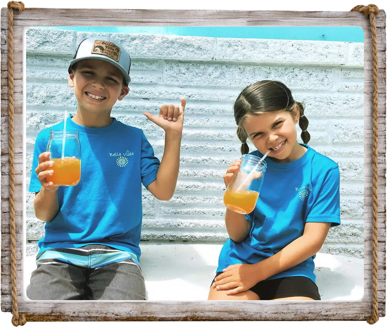 Two kids enjoying orange juice and smiling outdoors.