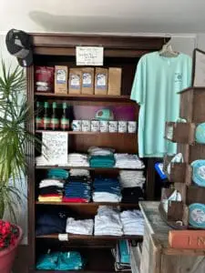 A retail shelf displaying folded clothes, bottled drinks, and hanging t-shirts.