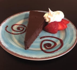 A slice of chocolate cake with whipped cream and strawberries on a decorative plate.