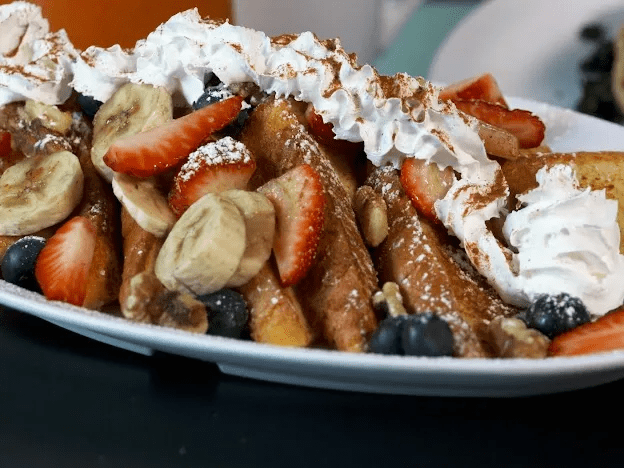 Plate of French toast topped with fruits and whipped cream.