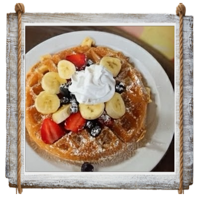 A waffle topped with bananas, strawberries, blueberries, and whipped cream.