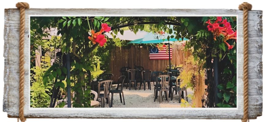 Outdoor seating area with black chairs and tables under a vine-covered pergola.