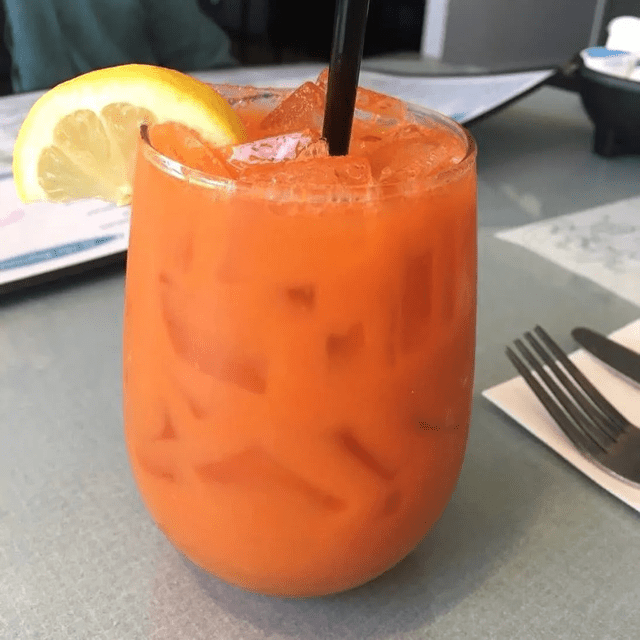 A refreshing iced Thai tea garnished with a lemon slice and a straw.