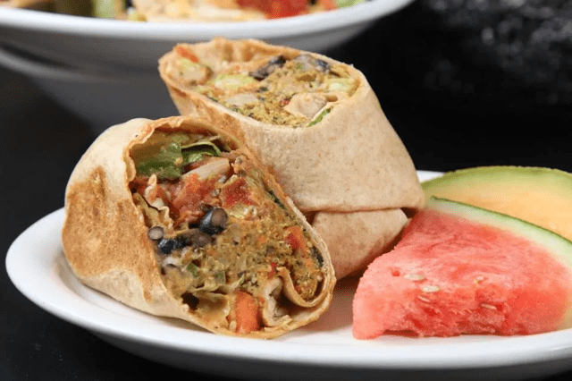 A close-up of a veggie wrap with watermelon slices on the side.