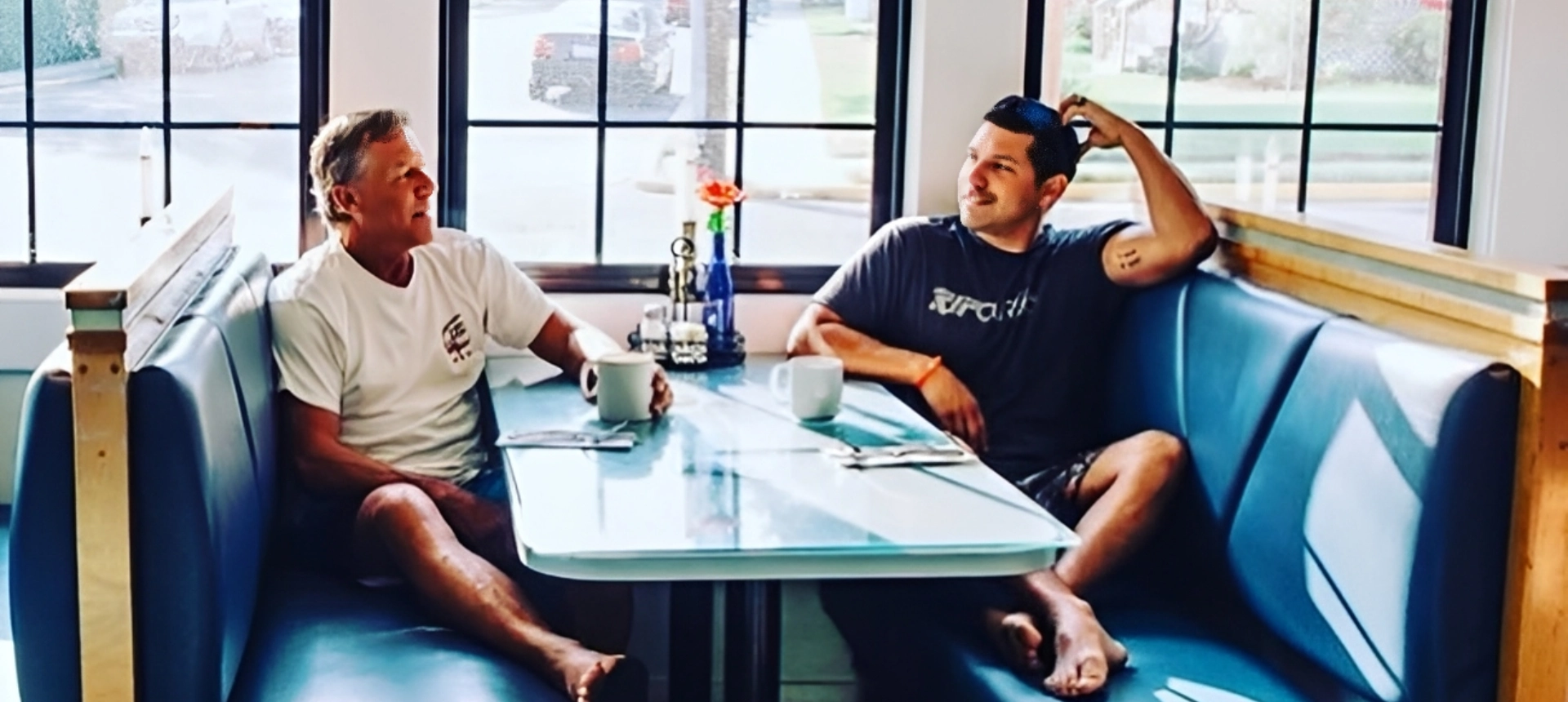 Two men sitting and chatting at a glass table by the window.